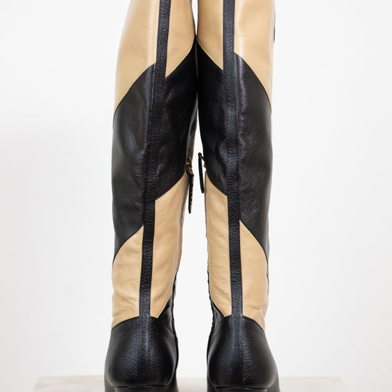 Back view of black and beige asymmetrical leather stripes of boot showing heel in back and standing against a white background