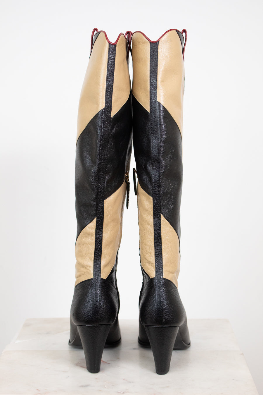 Back view of black and beige asymmetrical leather stripes of boot showing heel in back and standing against a white background
