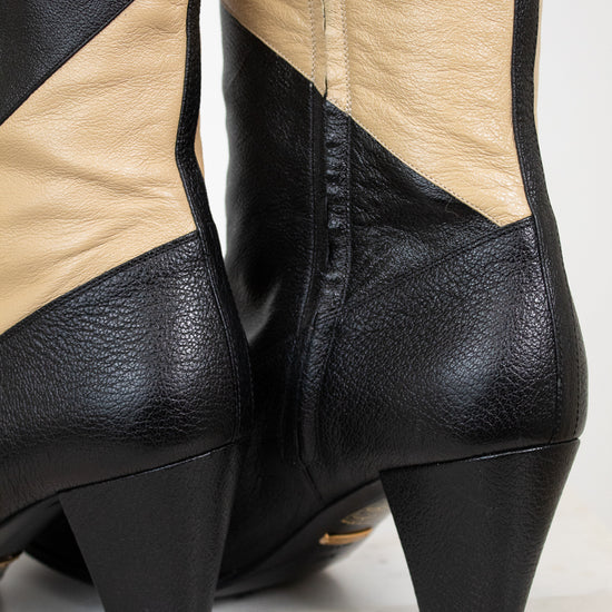 Close up of heel of black and beige striped leather boot standing on a plain marble surface