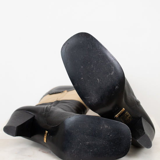 Sole view of black and beige boots showing minimal wear and laying against a plain marble background