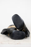 Sole view of black and beige boots showing minimal wear and laying against a plain marble background