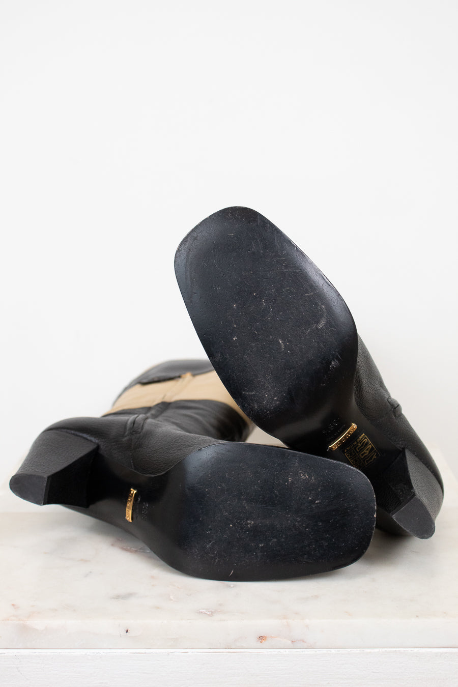Sole view of black and beige boots showing minimal wear and laying against a plain marble background