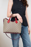Person holding a Gucci handbag with a beige pattern and red accents.