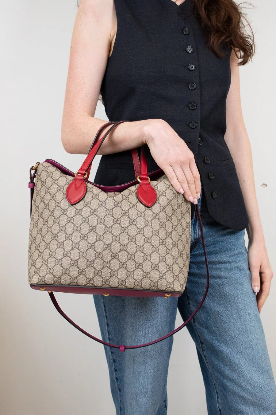 Person holding a Gucci handbag with a beige pattern and red accents.