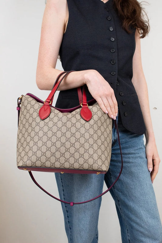 Person holding a Gucci handbag with a beige pattern and red accents.