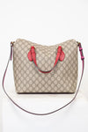 Beige handbag with red handles and a black strap on a white background