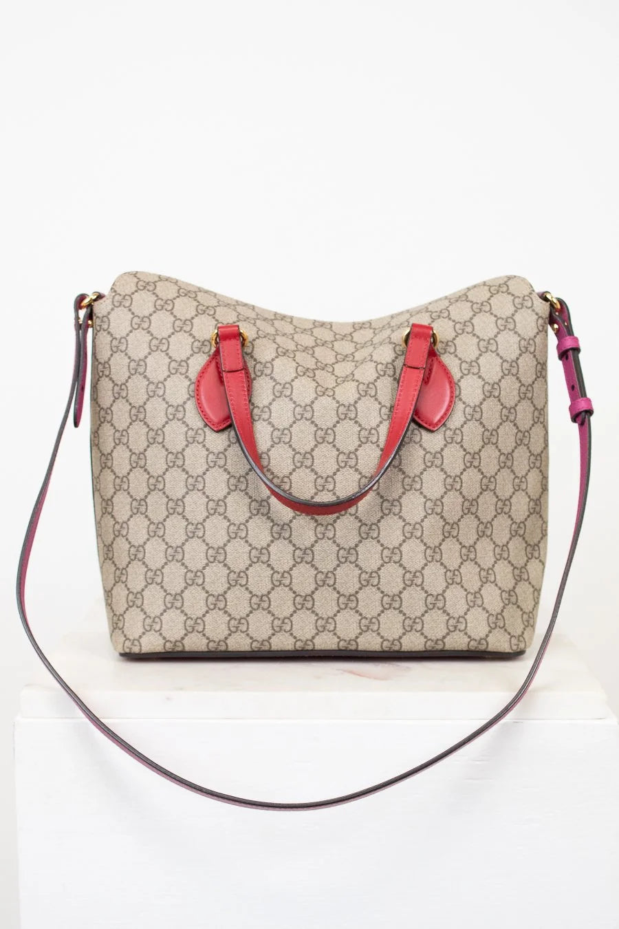 Beige handbag with red handles and a black strap on a white background