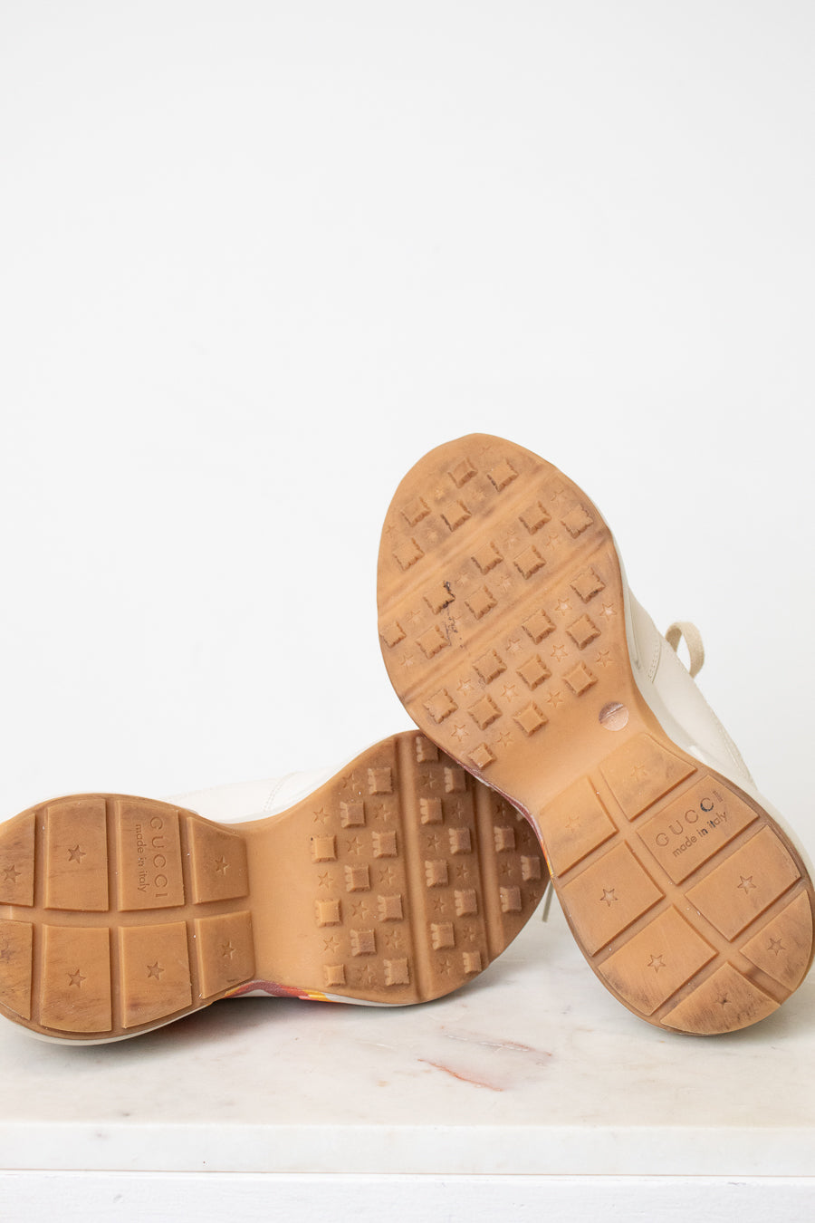 Close-up of the tan rubber soles of a pair of shoes, showing tread patterns and size markings, photographed against a plain white background.