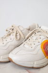 A white leather sneaker featuring a red, orange, and yellow graphic on the side with a stylized interlocking G logo, set against a plain white background.