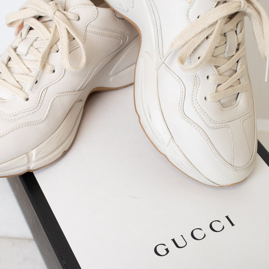 A white leather sneaker set against a white and black "Gucci" box
