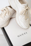A white leather sneaker set against a white and black "Gucci" box