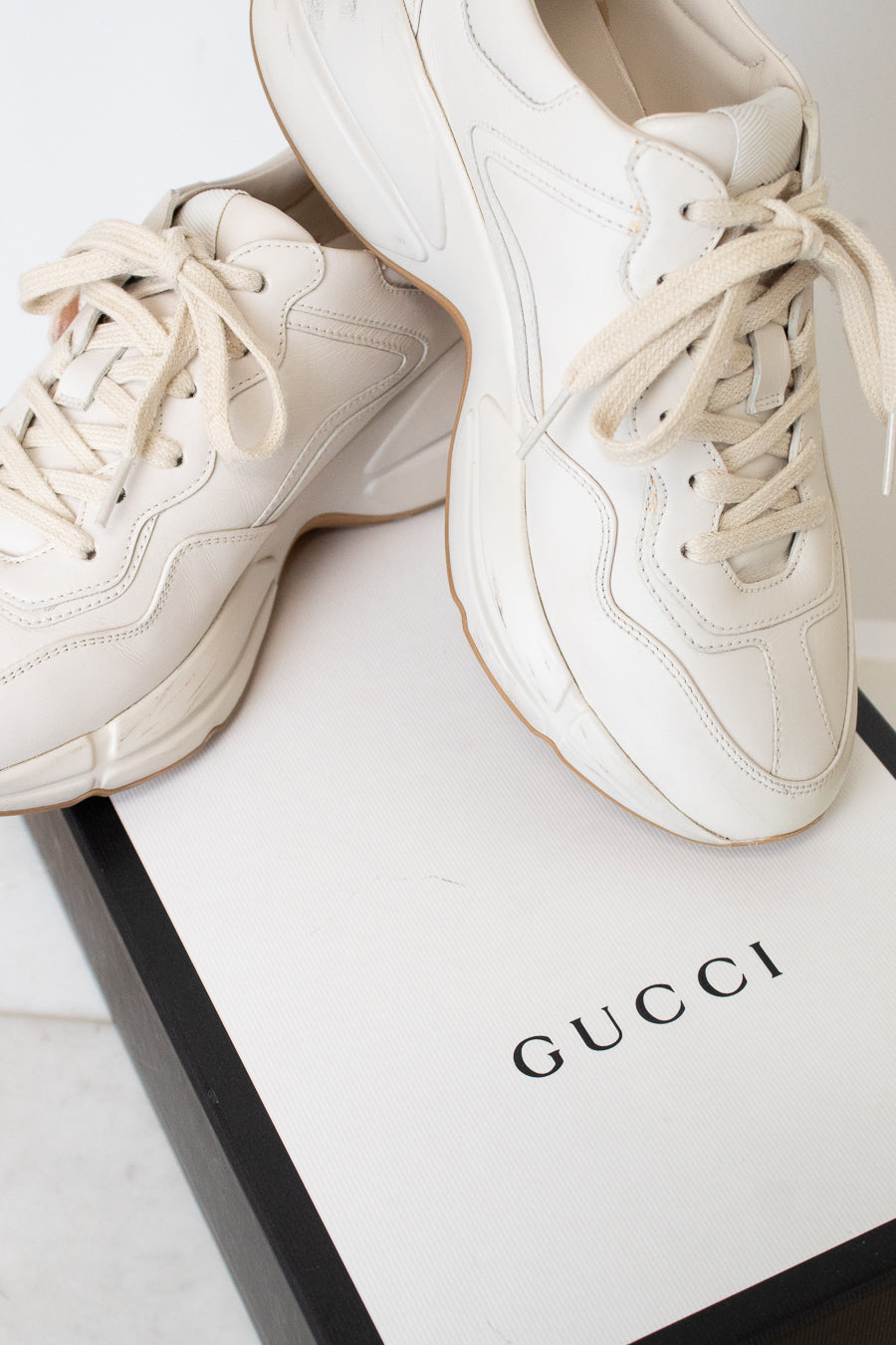A white leather sneaker set against a white and black "Gucci" box