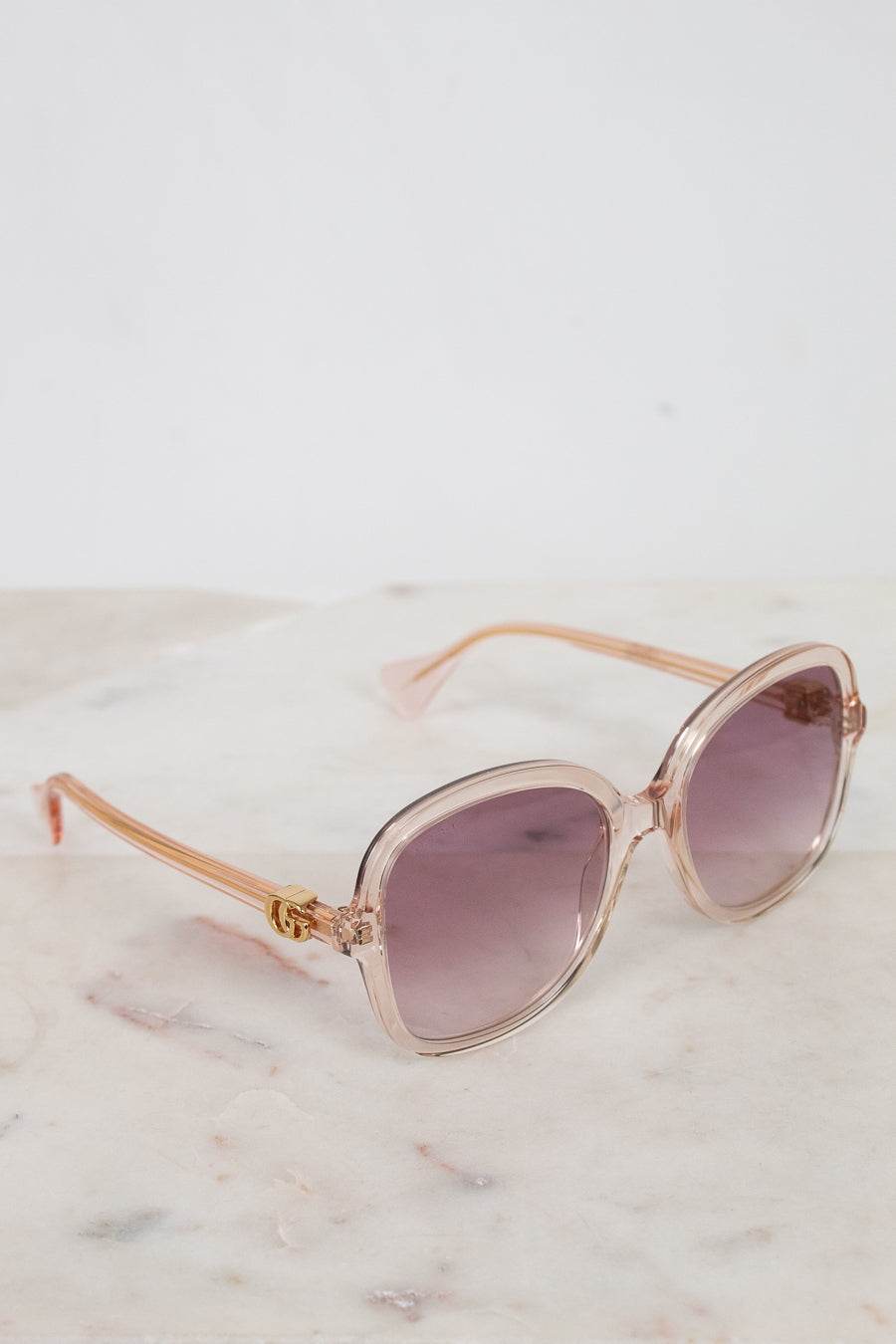Rose gold sunglasses with pink gradient lenses on a marble surface
