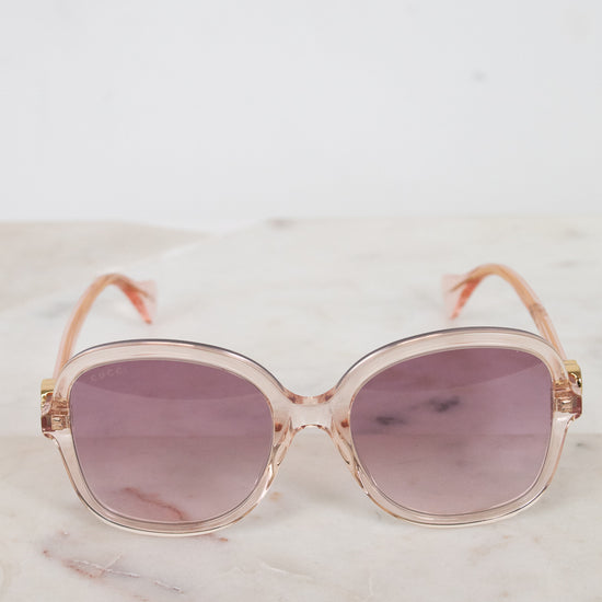 Sunglasses with a pink tinted frame and purple lenses on a marble surface