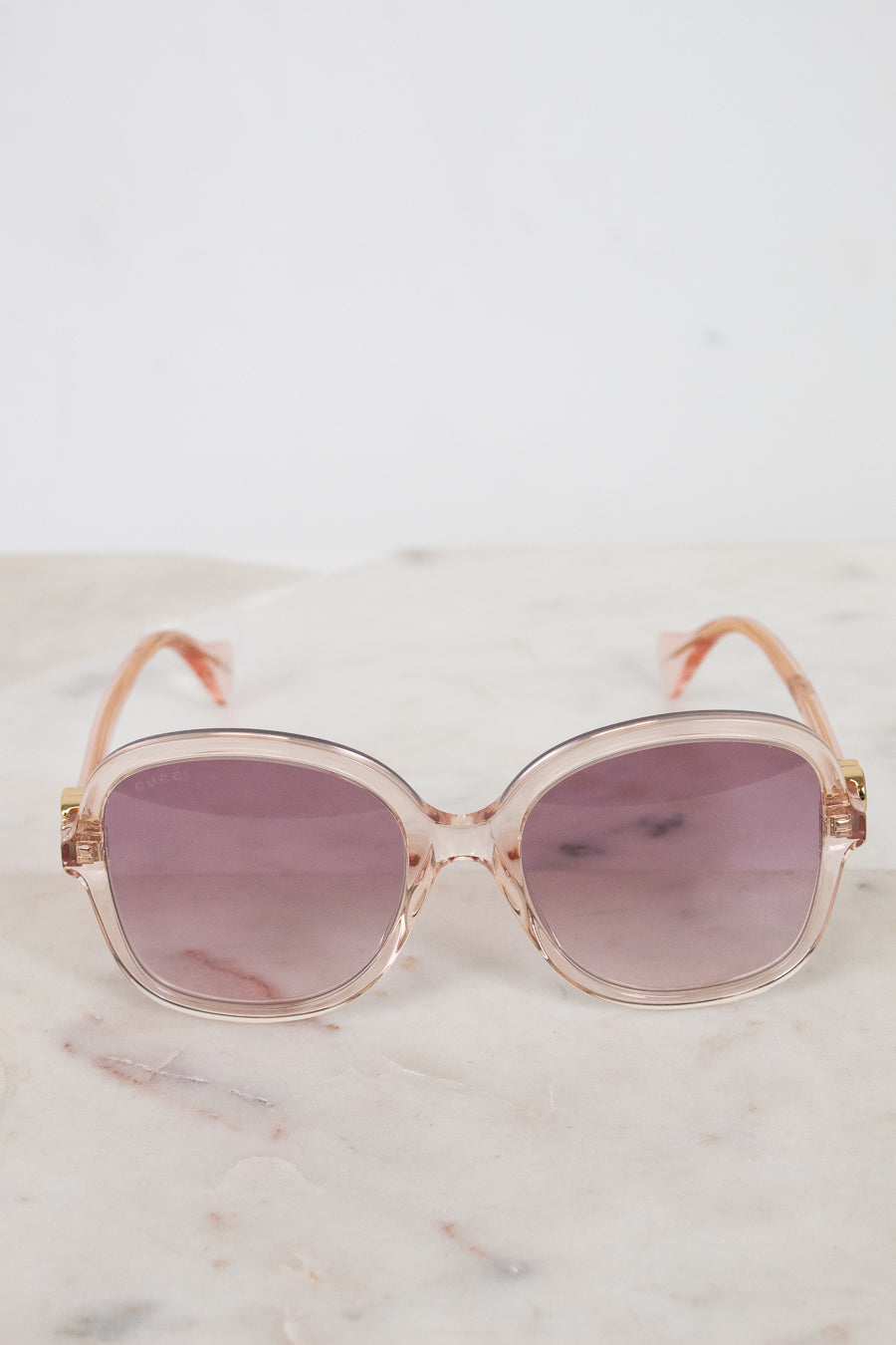 Sunglasses with a pink tinted frame and purple lenses on a marble surface