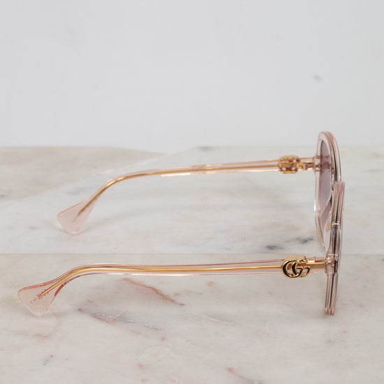 Gold-detail framed sunglasses with pink frames and lenses on a marble surface