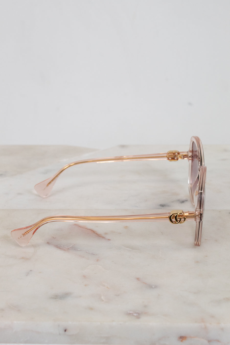 Gold-detail framed sunglasses with pink frames and lenses on a marble surface