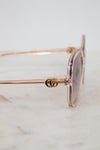 Gold-detail framed pink tinted sunglasses with a Gucci logo on a marble surface
