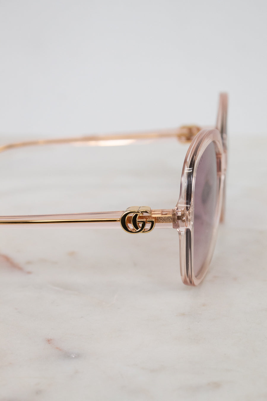 Gold-detail framed pink tinted sunglasses with a Gucci logo on a marble surface