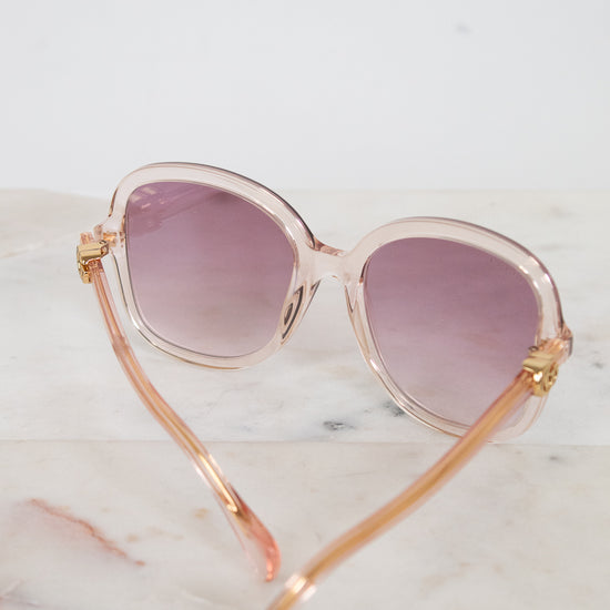 Sunglasses with pink and gold frame and pink lenses on a marble surface