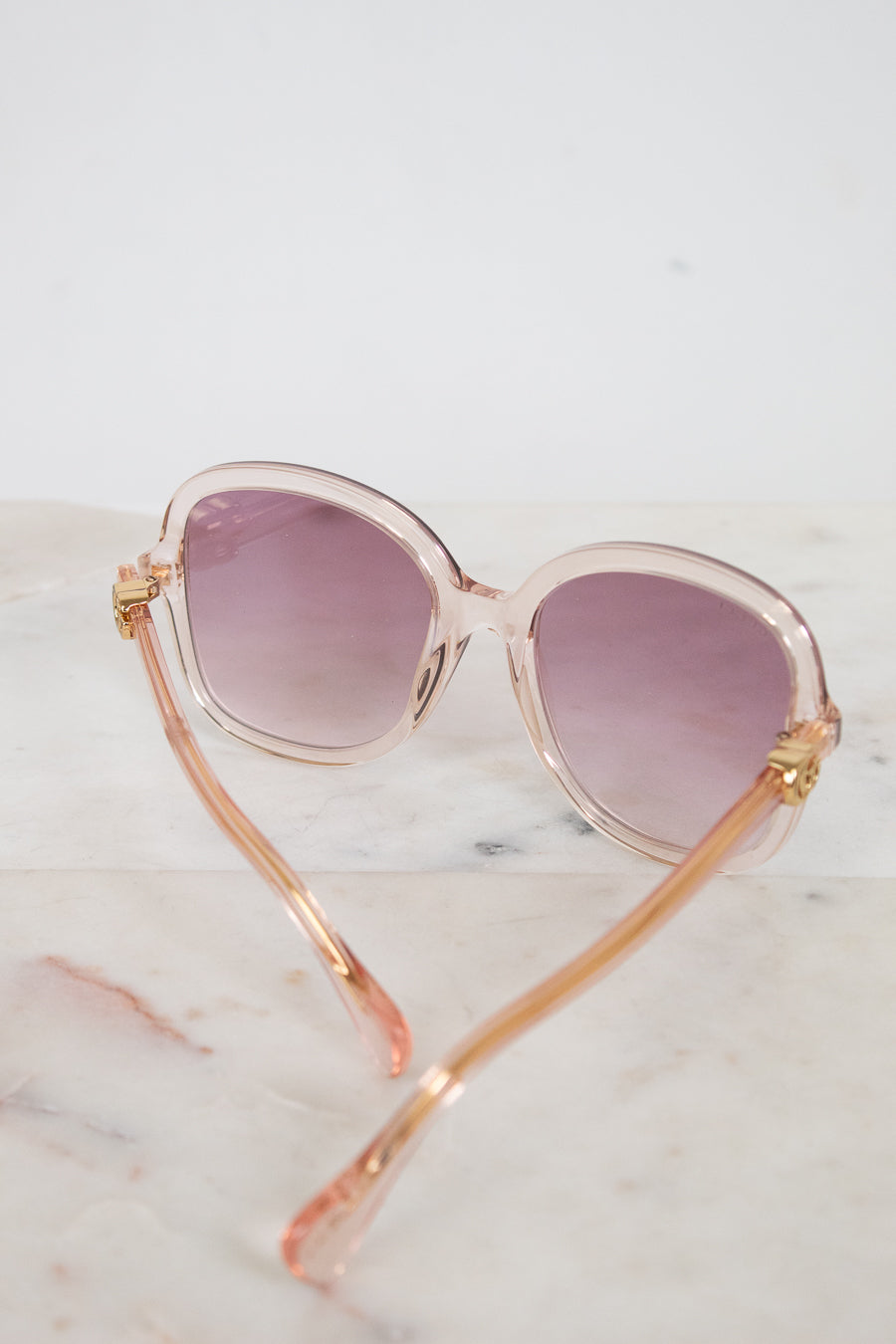 Sunglasses with pink and gold frame and pink lenses on a marble surface