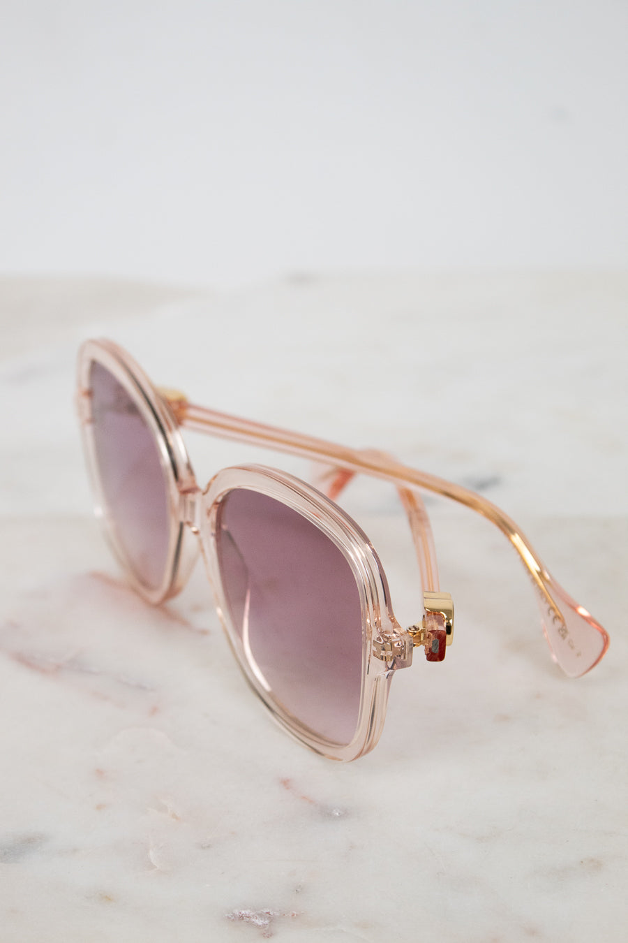 Pink and gold sunglasses with pink gradient lenses on a marble surface