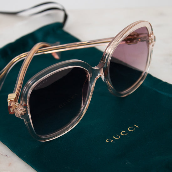 Sunglasses with pink frame and dark pink lenses on a Gucci green pouch.