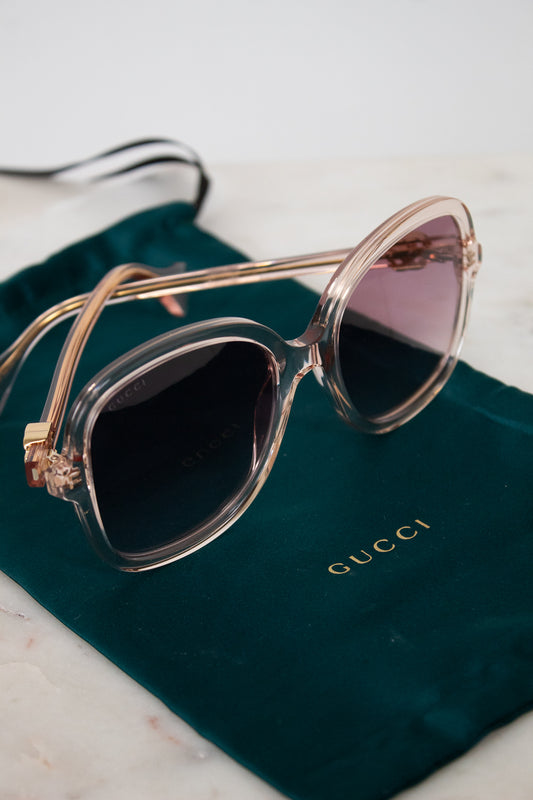 Sunglasses with pink frame and dark pink lenses on a Gucci green pouch.