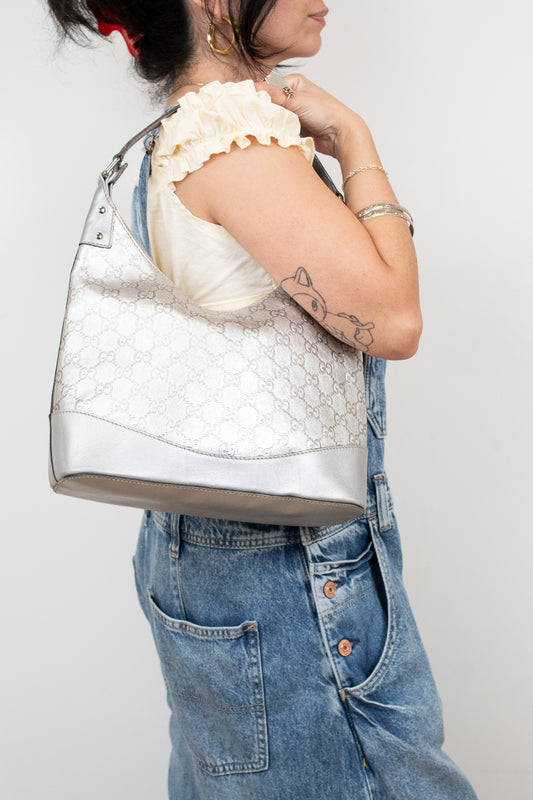Person holding a textured silver handbag against a plain background