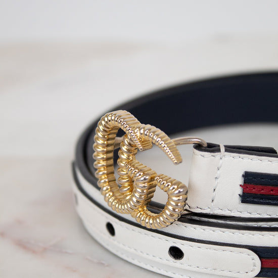 White leather belt with gold buckle on a marble surface