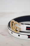 White leather belt with gold buckle on a marble surface