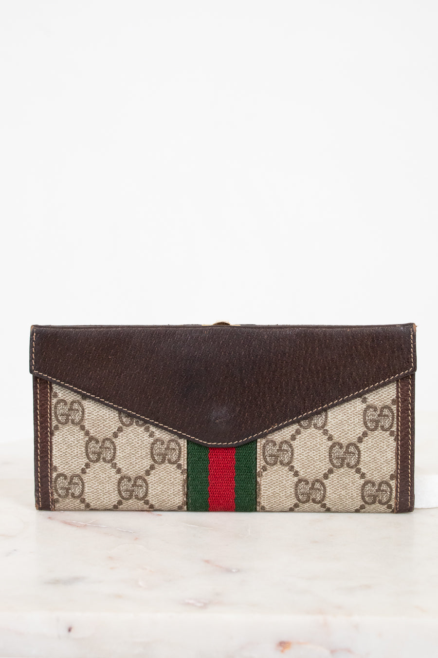 Designer wallet with dark brown leather flap and patterned body on a white background