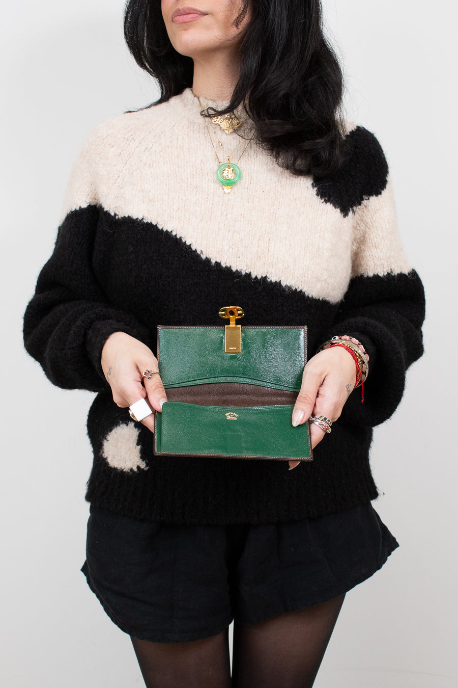 Person wearing a black and white sweater holding a green wallet against a plain background