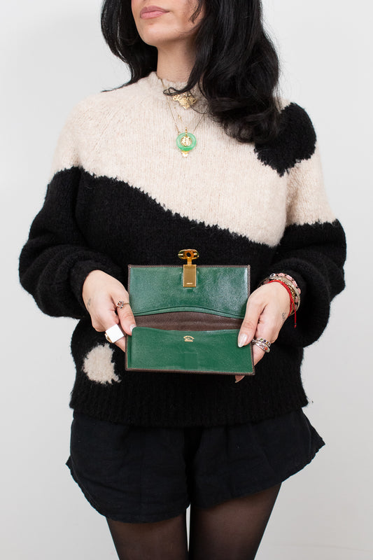 Person wearing a black and white sweater holding a green wallet against a plain background