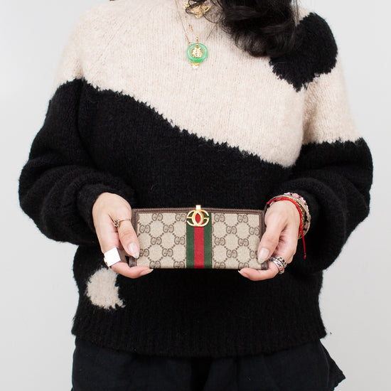 Person wearing a black and white sweater holding a Gucci wallet against a plain background