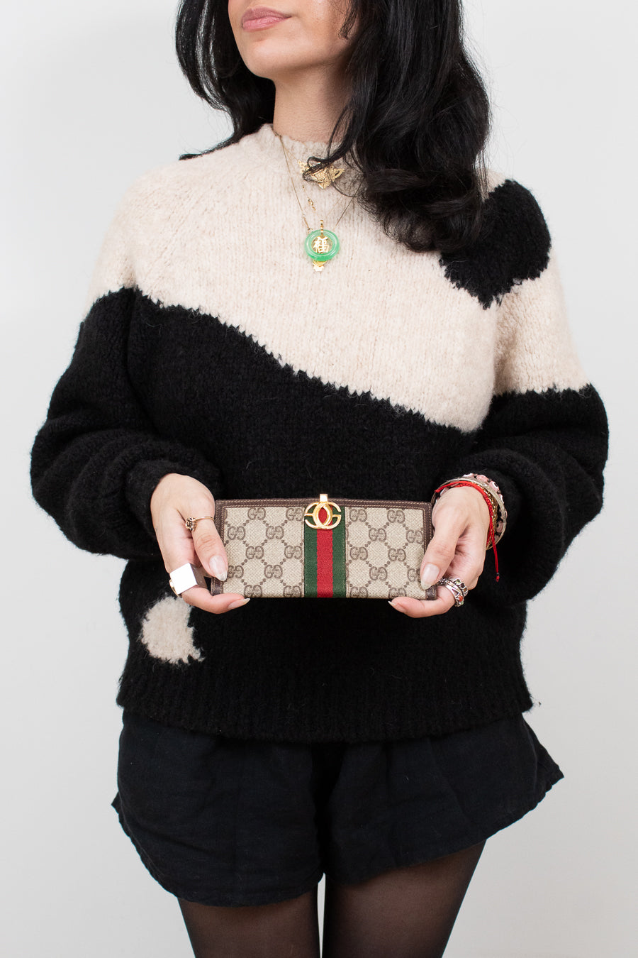 Person wearing a black and white sweater holding a Gucci wallet against a plain background
