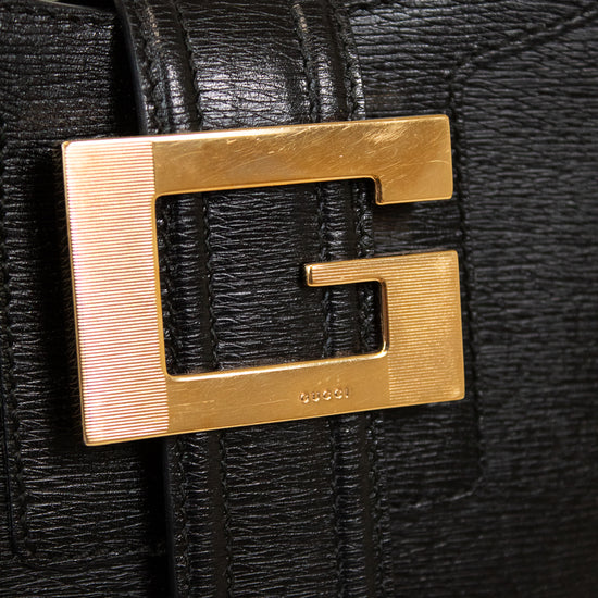 Black textured handbag with a gold logo on a light gray background
