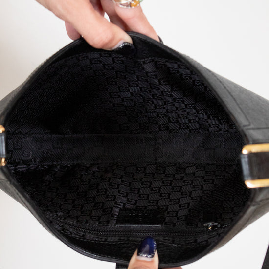 Black handbag with gold accents held open by a hand against a white background