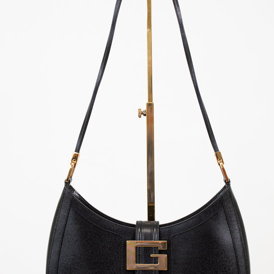 Black shoulder bag on gold stand with white background