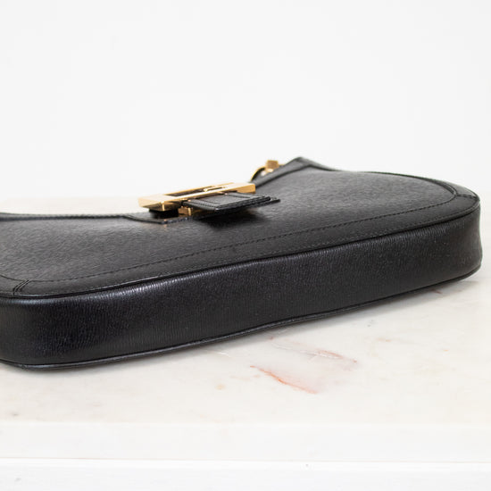 Black leather handbag with gold clasp on a light background