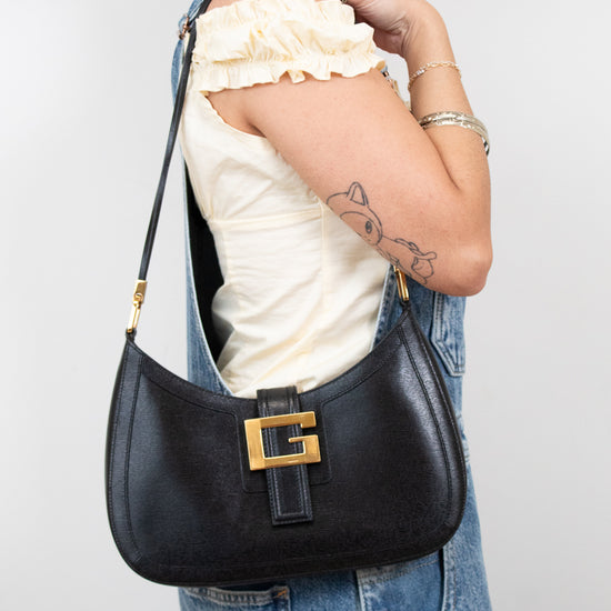 Person wearing overalls holding black shoulder bag with a white background