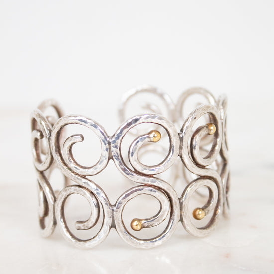 Silver cuff bracelet with gold accents on a white background