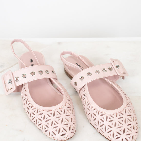 A pair of light pink slingback flats with geometric cutout detailing on the toe and side, featuring a decorative strap with silver studs on a white marble surface.