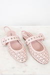 A pair of light pink slingback flats with geometric cutout detailing on the toe and side, featuring a decorative strap with silver studs on a white marble surface.
