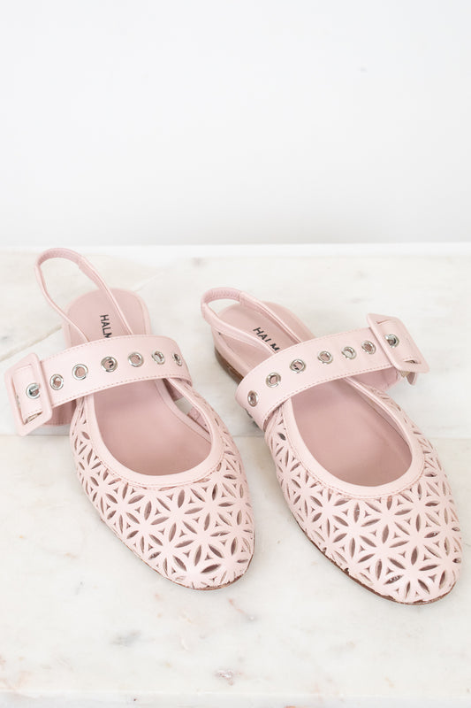 A pair of light pink slingback flats with geometric cutout detailing on the toe and side, featuring a decorative strap with silver studs on a white marble surface.