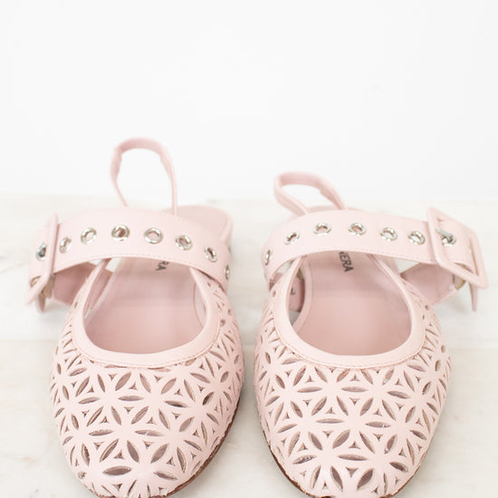 A pair of light pink baby ballet flats with geometric laser-cut patterns, studded straps, and bow details, displayed on a light marble surface against a white background.