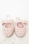 A pair of light pink baby ballet flats with geometric laser-cut patterns, studded straps, and bow details, displayed on a light marble surface against a white background.