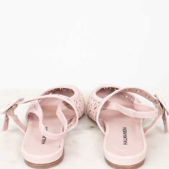 A pair of light pink flat sandals with cutout details and adjustable straps, shown from the back on a white marble surface against a white background.