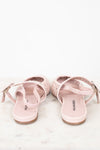 A pair of light pink flat sandals with cutout details and adjustable straps, shown from the back on a white marble surface against a white background.
