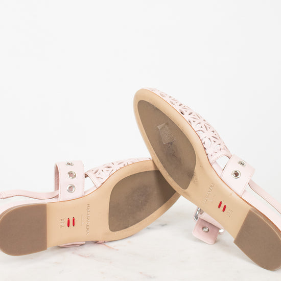 A pair of light pink leather flat sandals with laser-cut geometric patterns on the toe straps, displayed on a white marble surface against a white background.